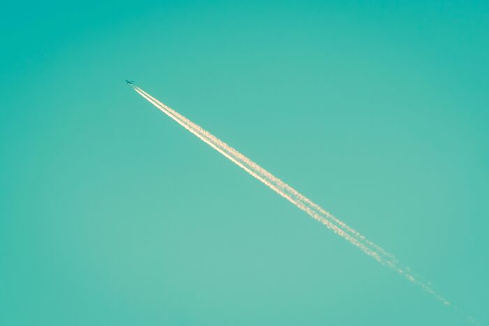 Airplane flying in clear sky with contrails, illustrating totally safe things that people can’t stop freaking out about.