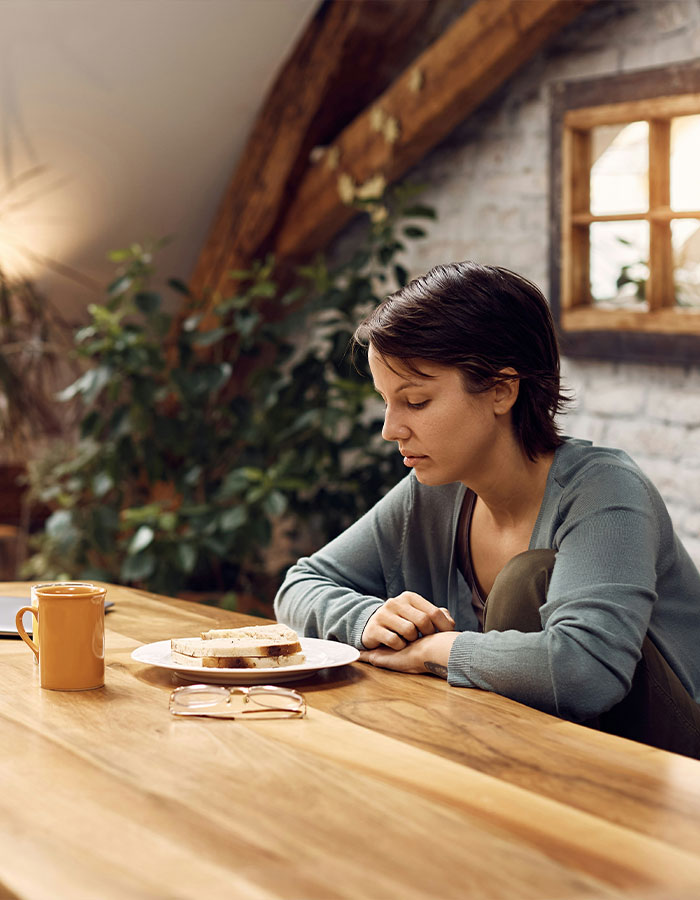 Young woman sitting at a wooden table, looking down sadly at her untouched sandwich, reflecting pain from a rare disorder. Young woman sitting at a wooden table, looking down sadly at her untouched sandwich, reflecting pain from a rare disorder.