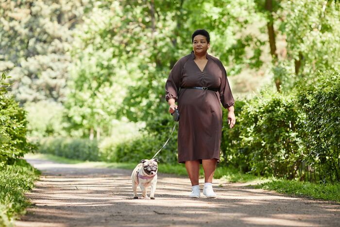 Woman walking a dog on a path in a park, representing tips from ex-fat people on how to lose weight.
