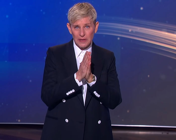 Ellen DeGeneres in a black suit, with hands clasped, addressing audience amid bullying controversy claims on stage. Ellen DeGeneres in a black suit, with hands clasped, addressing audience amid bullying controversy claims on stage.