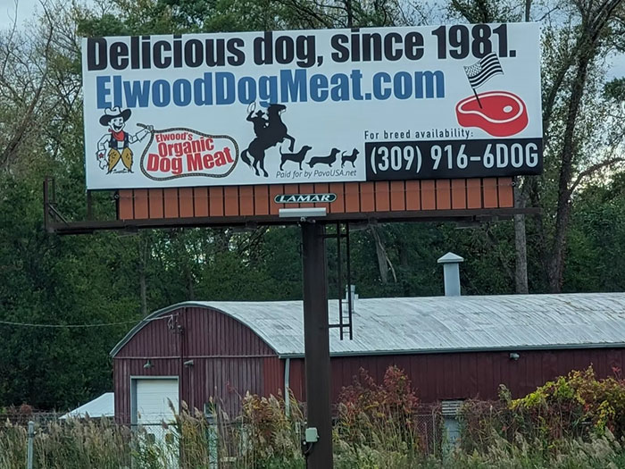 Billboard advertisement for Elwood Dog Meat farm displaying contact info and promoting dog meat since 1981 amid rural setting. - 6