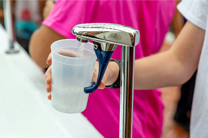 Patient filling a disposable cup with water from a medical hydration station in an emergency room setting.