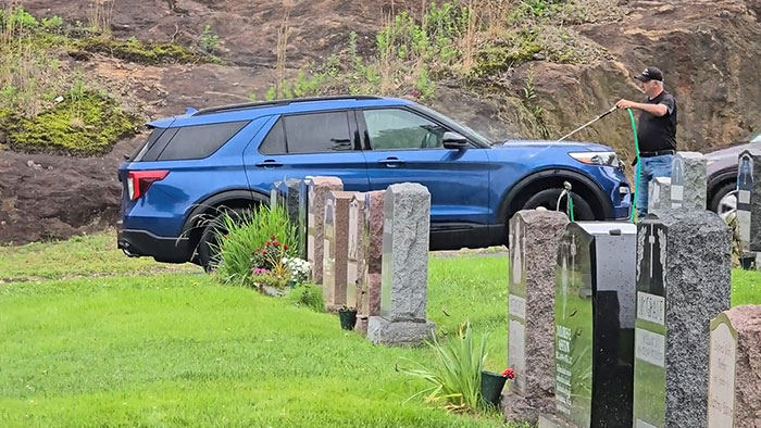 Man washing a blue SUV illegally parked in a cemetery, showing blatant disregard for rules and etiquette.