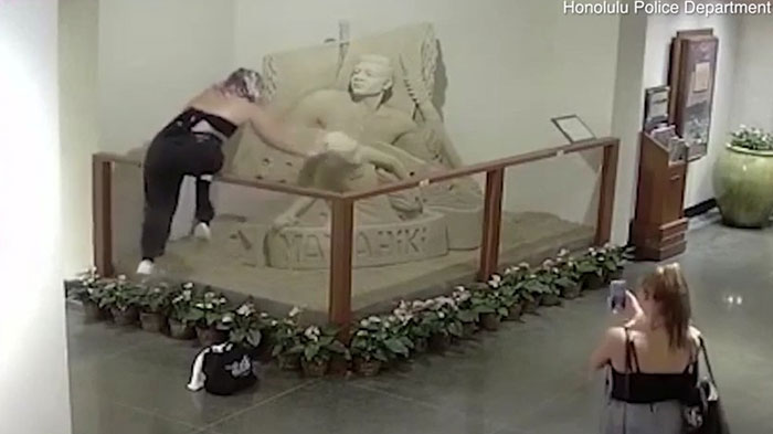 Person vandalizing a statue inside a museum, showing blatant disregard for rules and etiquette in a public space.