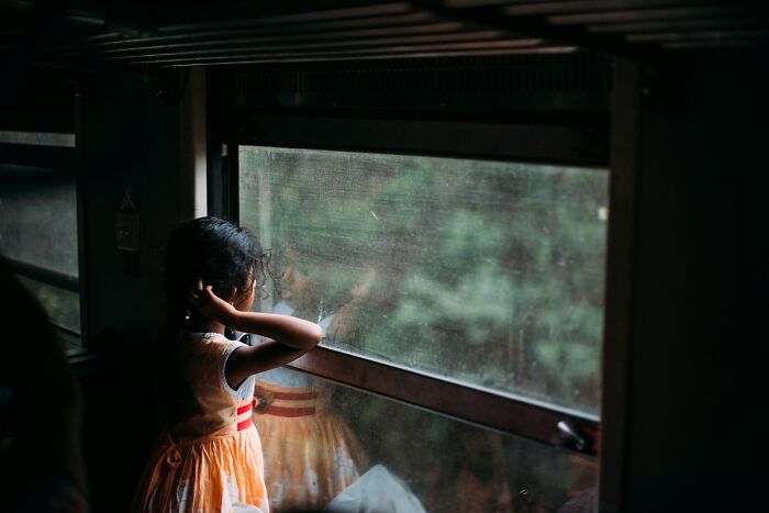 Young girl in an orange dress looking out a window with a thoughtful expression, portraying creepy and terrifying imaginary friends.
