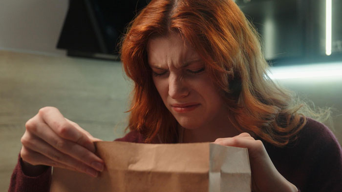 A red-haired woman displaying a pained expression while opening a brown paper bag, reflecting betrayal and revenge feelings. - 13