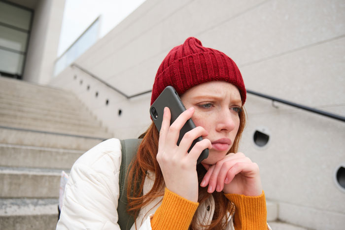 Young woman in red beanie looking troubled while talking on phone, reflecting feelings of betrayal and revenge. - 9