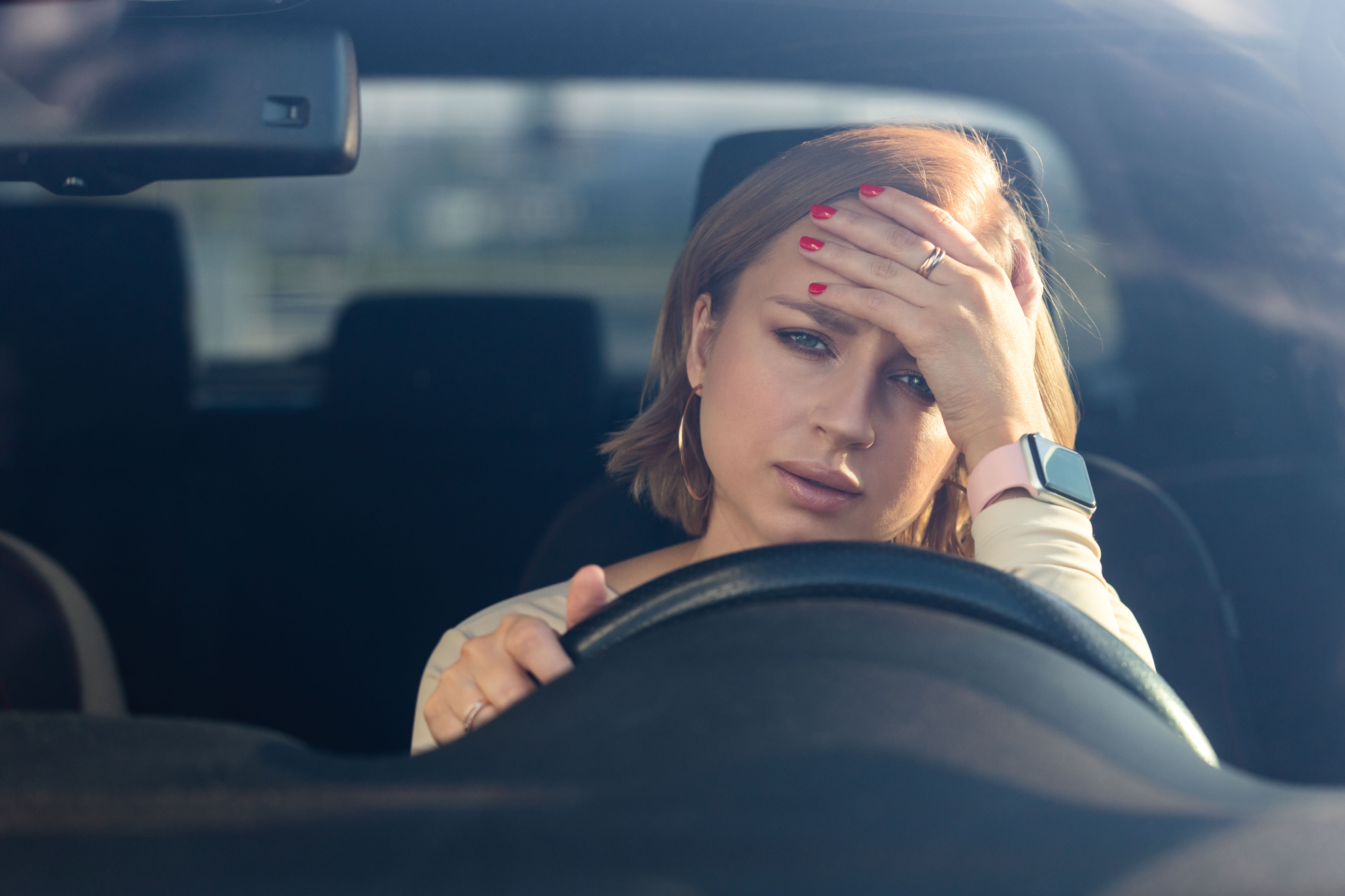 Frustrated woman holding her forehead while driving a car, depicting road trip stress and sibling conflict. Frustrated woman holding her forehead while driving a car, depicting road trip stress and sibling conflict.