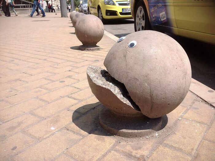Concrete street bollards designed with eyes and open mouths, creative street art blurring urban function and playful sculpture.