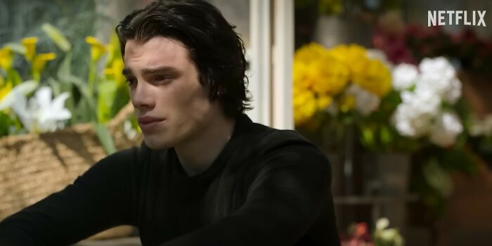 Young man with dark hair wearing black shirt, sitting indoors near bright flowers, representing Netflix movies that disappointed viewers.