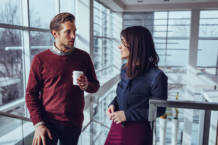 Two coworkers in a modern office having a serious conversation, illustrating a person calling obnoxious coworker's bluff.