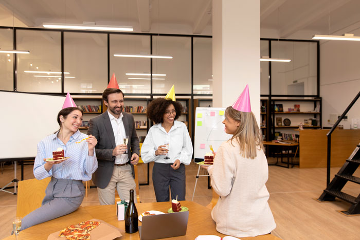 Coworkers celebrating with cake and drinks at a surprise retirement party in an office setting.