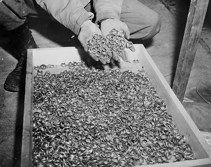 Man holding a large collection of metal rings over a tray filled with rings in a historical photo.