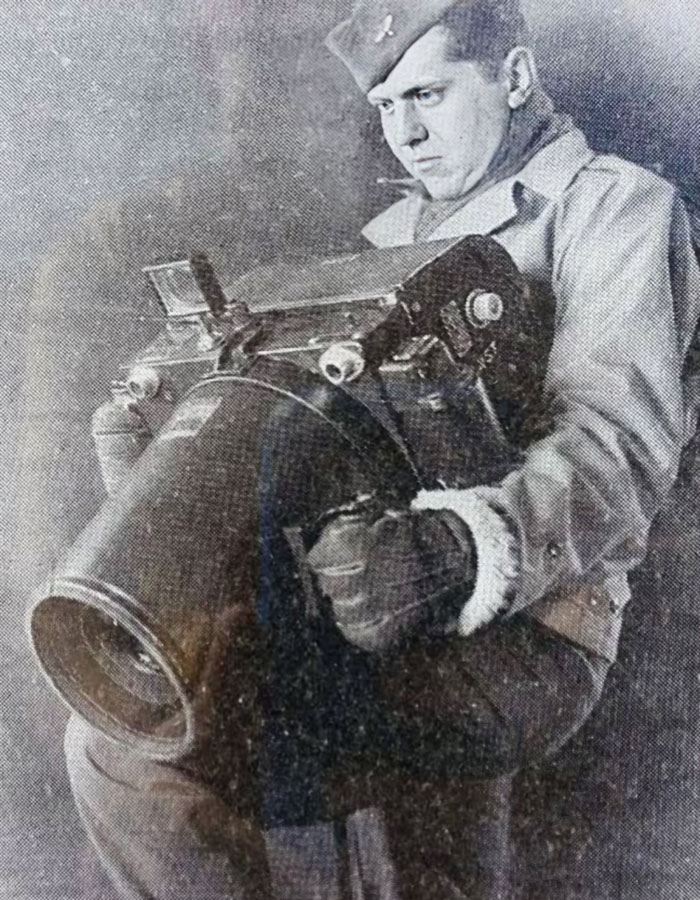 Black and white historical photo of a man holding an unusually large vintage camera device from the past.