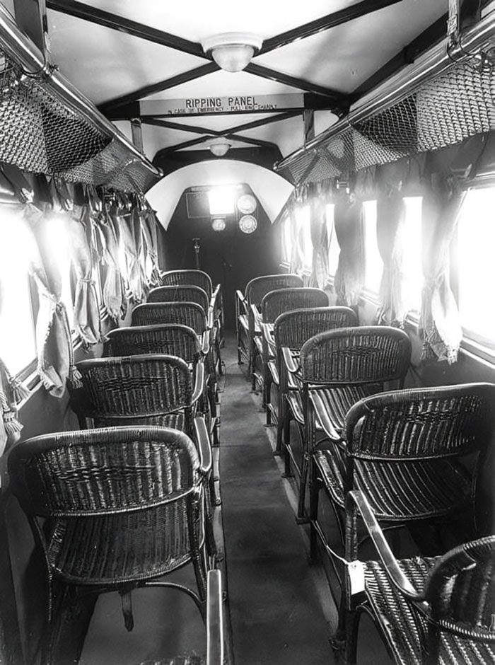Interior view of a historical train car with wicker seats and sunlight streaming through lace curtains.