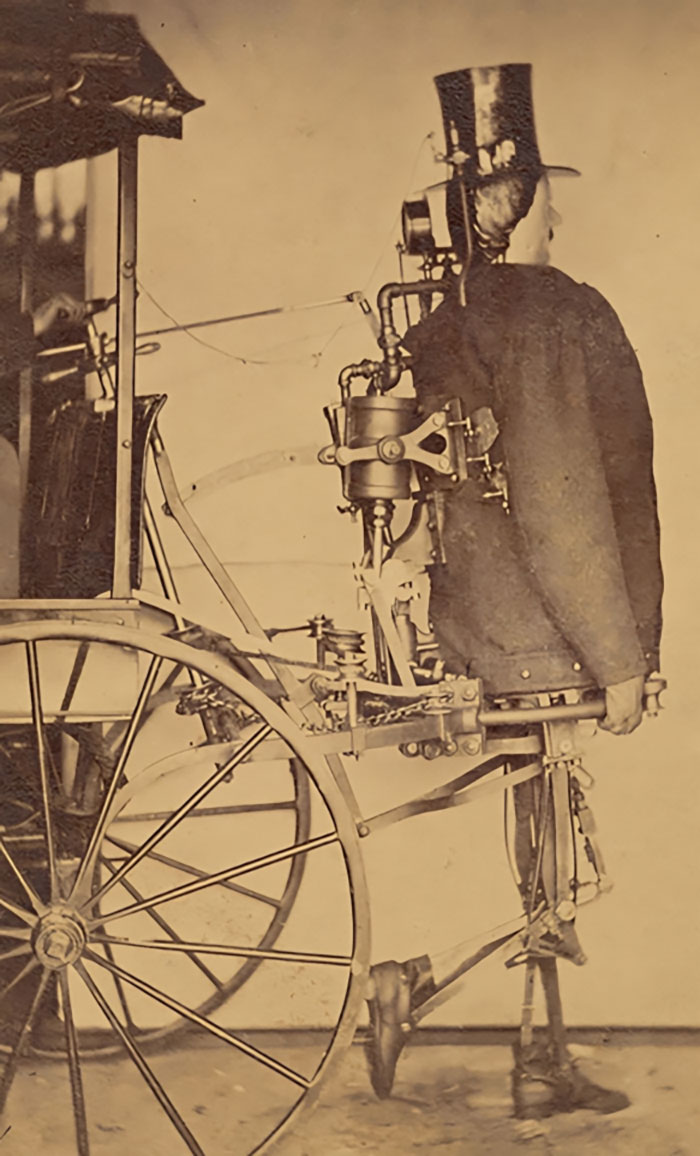 Vintage historical photo of a man wearing a mechanical apparatus attached to a cart, showcasing early invention technology.