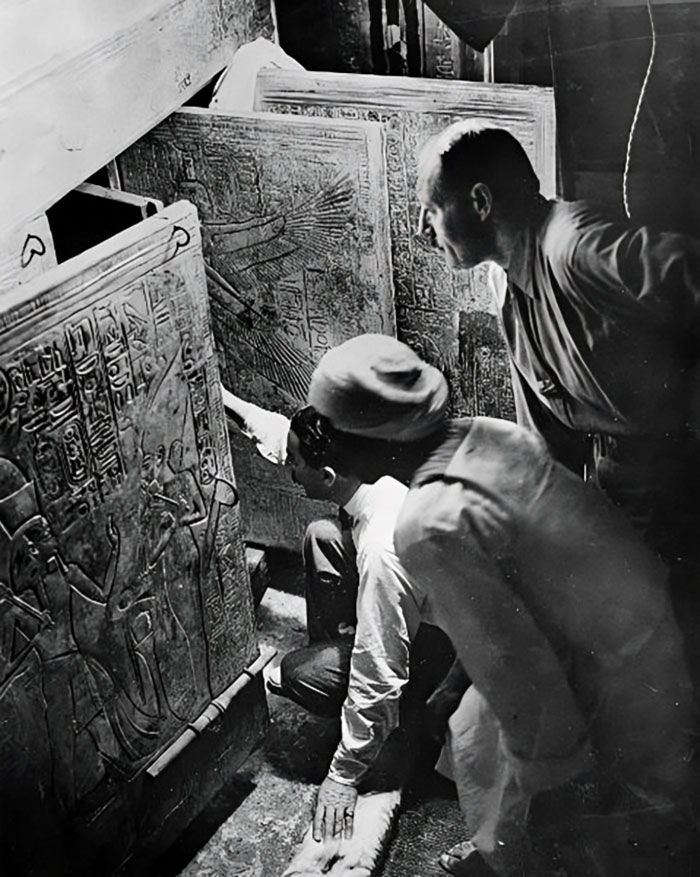 Three men examining ancient Egyptian hieroglyphs carved into stone in a historical photo with archaeological significance.