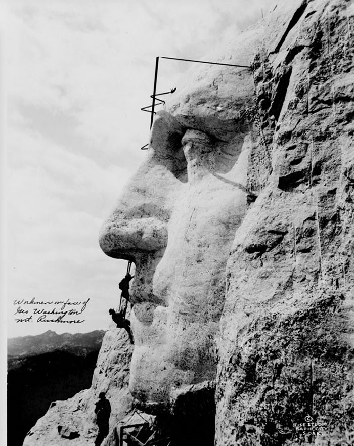 Workmen scaling the unfinished Mount Rushmore carving, a unique historical photo capturing the creation process.