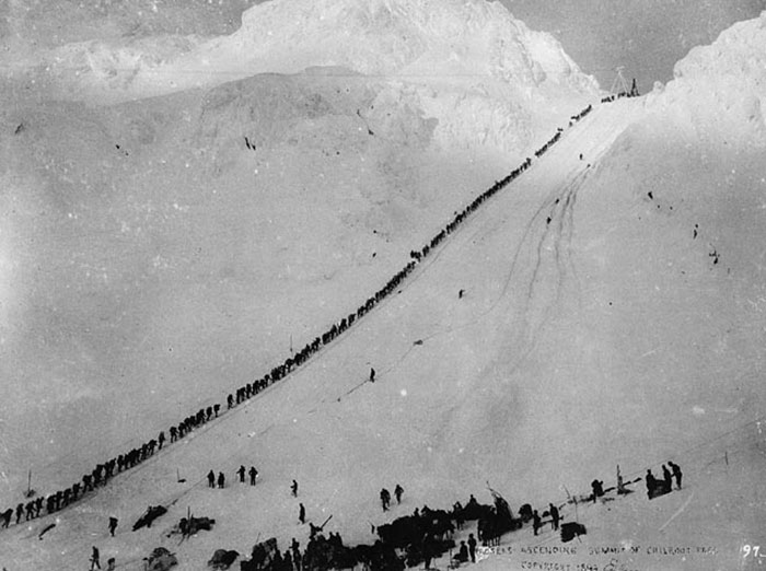 Long line of climbers ascending a snowy mountain slope in a rare historical photo with unusual and wild challenges.