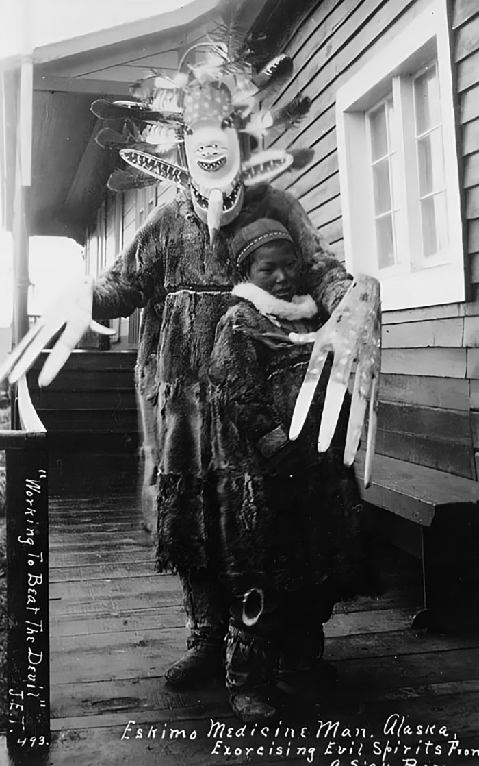 Eskimo medicine man in traditional costume performing ritual to exorcise evil spirits in historical photo