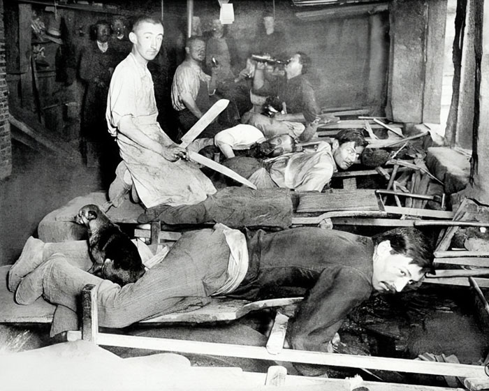 Men bound face down on wooden frames with others standing, holding swords, in a bizarre historical photo scene.