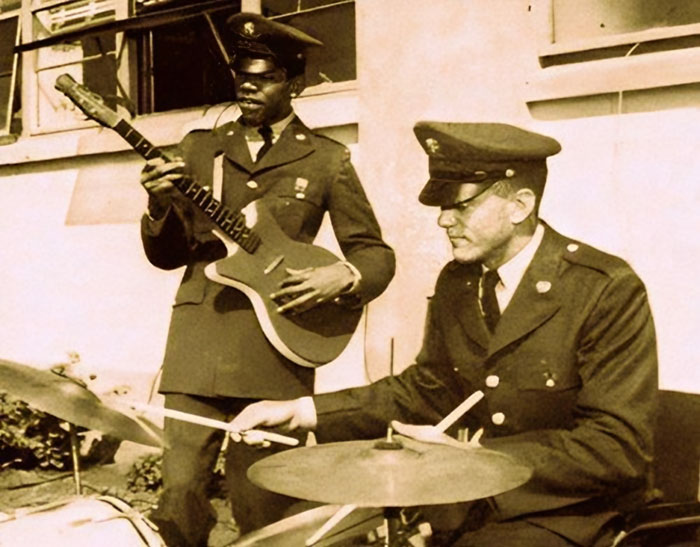 Two soldiers in uniform playing guitar and drums in a unique historical photo capturing a rare moment of music.