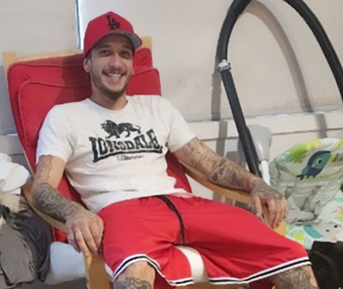 Young dad with tattoos sitting on red chair smiling, related to news about dad losing life after being buried alive.
