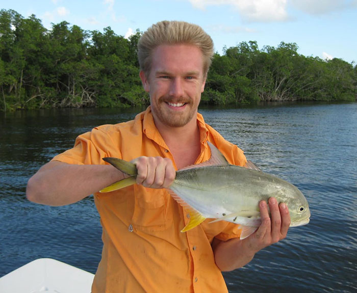 Man holding a fish by the water, related to tragic dad who lost life after being buried alive while digging sand with kids.