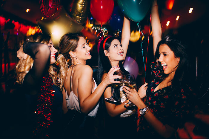 Group of young women celebrating at night party with balloons and drinks, highlighting wealth gap perspective and lifestyle contrast.