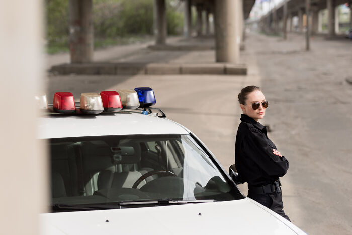 Police officer standing by patrol car under a bridge, illustrating creepy and disturbing things police officers saw at homes.