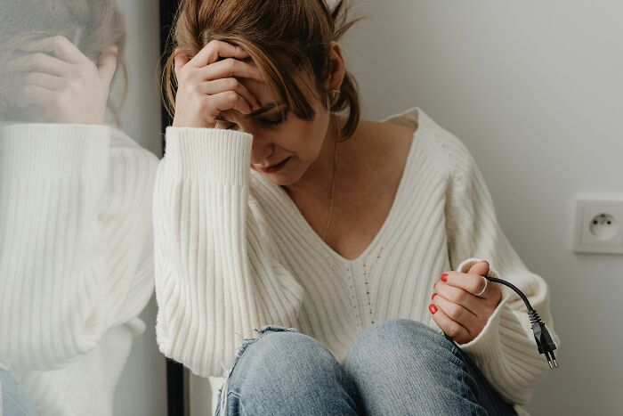 Woman sitting on the floor stressed, holding a power plug, symbolizing emotional struggle with fiance non biological child wedding issues.