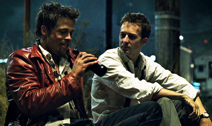 Two men sitting outdoors at night, one drinking from a bottle, depicting a moment related to NSFW stories shared online.