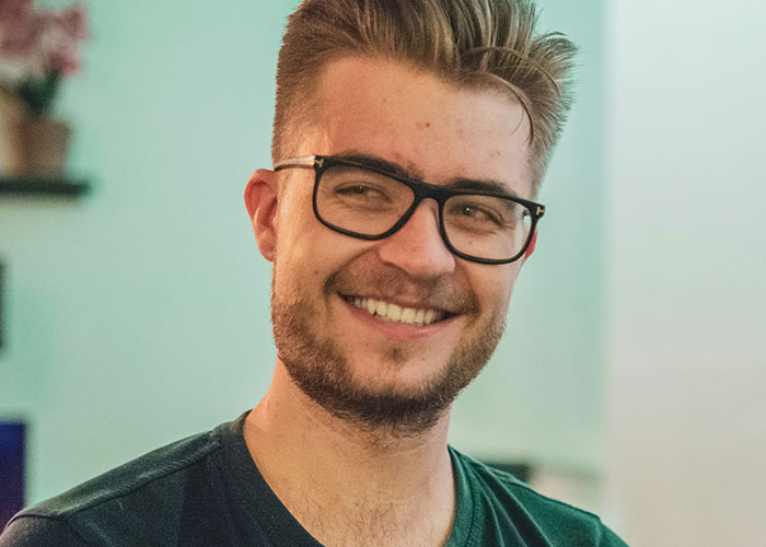 Smiling man with glasses indoors, illustrating the impact of banning flexible hours at work by a boss trying to fix a non-issue. Smiling man with glasses indoors, illustrating the impact of banning flexible hours at work by a boss trying to fix a non-issue.