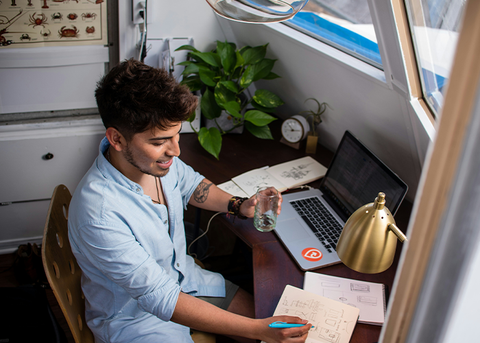 Young man working at home desk with laptop and notes, highlighting challenges of banning flexible hours by boss. Young man working at home desk with laptop and notes, highlighting challenges of banning flexible hours by boss.