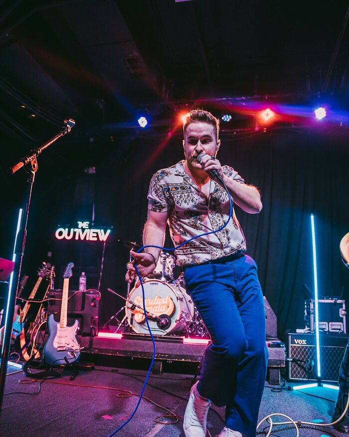 Man performing on stage with microphone in hand during a vibrant concert, highlighting struggles of short king in dating.