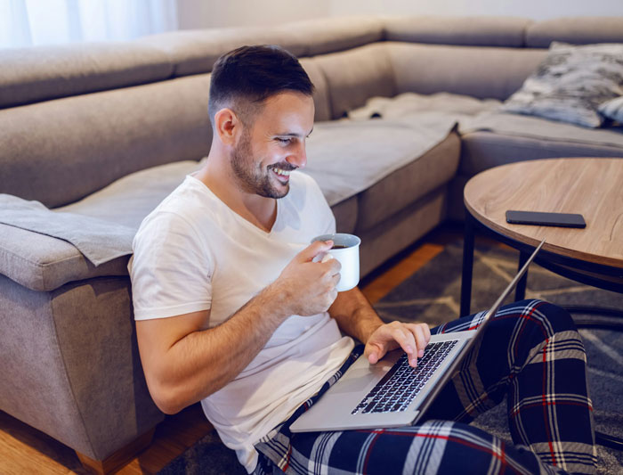 Grieving employee working on laptop at home, drinking coffee, showing resilience despite difficult boss behavior.