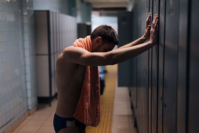 A shirtless inmate leaning against lockers in a dim prison hallway, illustrating life in prison challenges.