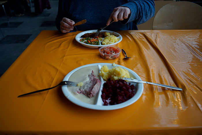 Prison inmate eating a meal with mashed potatoes, vegetables, and sliced meat on a tray in a prison dining hall.