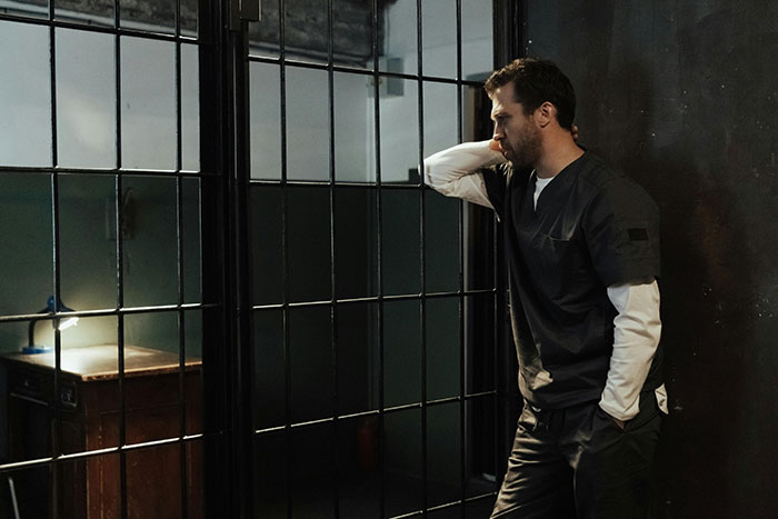 Man in prison uniform standing by bars, reflecting on the challenges of life in prison and its daily realities.