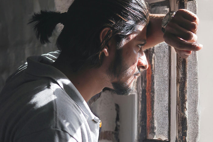 Young man in prison, looking out a small barred window, reflecting on life in prison challenges.