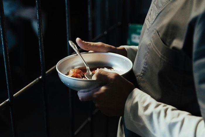 Inmate holding a bowl of prison food near bars, illustrating life in prison hardships and daily struggles inside jail.