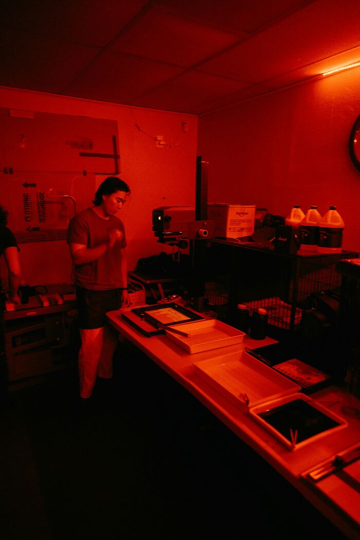 Night shift worker in a dark red-lit room processing photos, evoking a chilling paranormal encounter atmosphere.