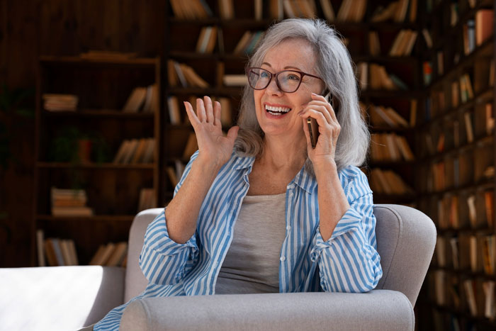 Older woman smiling and waving during a phone call, enjoying free salon service marriage consultation at home. Older woman smiling and waving during a phone call, enjoying free salon service marriage consultation at home.