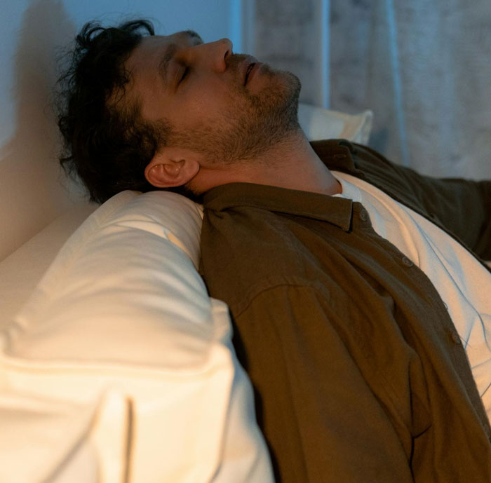 Man leaning back on sofa with eyes closed, illustrating friend break into house scenario with planted belongings.