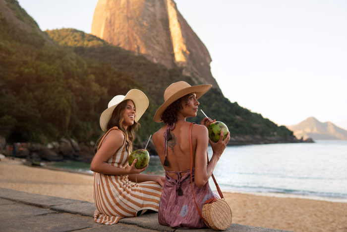 Two women enjoying a beach view, sipping coconuts, capturing the theme of woman wants friends to bend for travel needs.