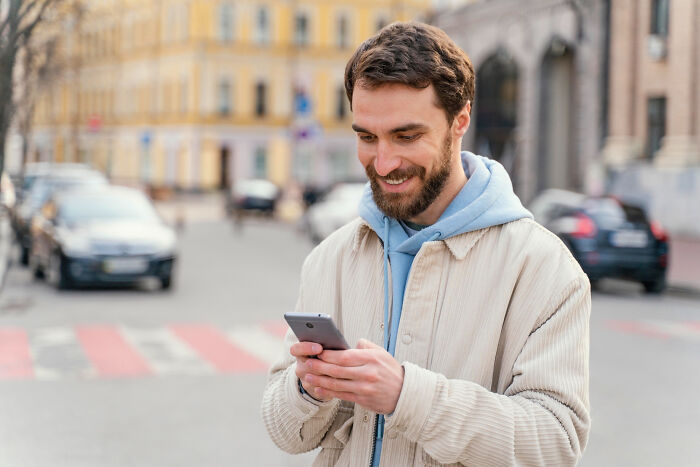 Man smiling and using a smartphone outdoors, illustrating friend stop messaging and changing friendship dynamics.