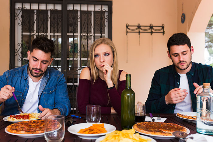 Three people sit silently at a tense dinner table, reflecting chaos after racist insults at a family gathering.