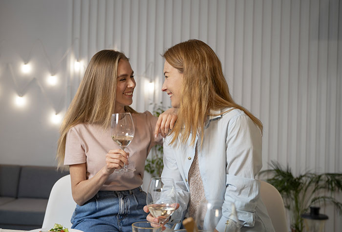 Two women smiling and socializing over wine, depicting confusion and tension after a test involving boyfriend&rsquo;s sister.