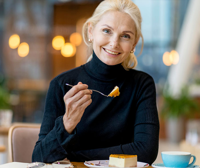 Smiling woman enjoying dessert in a caf&eacute;, illustrating man's compliment to girlfriend's mom causing family conflict.