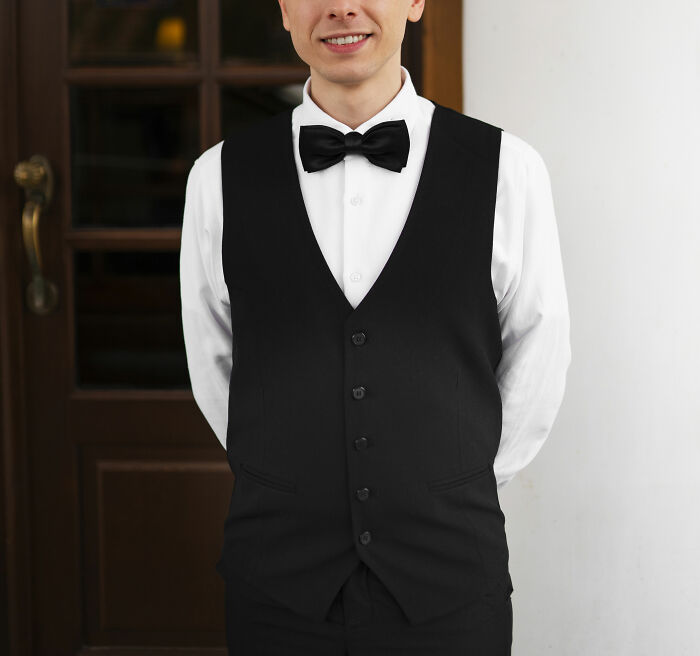 Young man in a black vest and bow tie standing with hands behind back, illustrating wealth gap perspective concept.